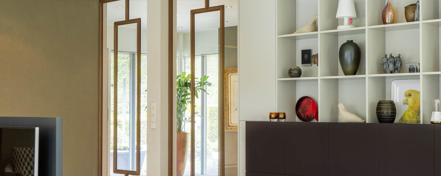 Dubbele bronzen stalen deuren met glas als elegante scheiding tussen hal en woonkamer.